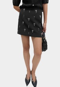 Schwarzer Minirock mit silbernem floralen Schmuck, kombiniert mit spitzen schwarzen Ballerinas und einer strukturierten schwarzen Handtasche.