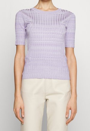 Kvinde iført en tætsiddende lavendelfarvet ribstrikket top med korte ærmer og cremefarvede bukser, vist fra skuldre til hofter.