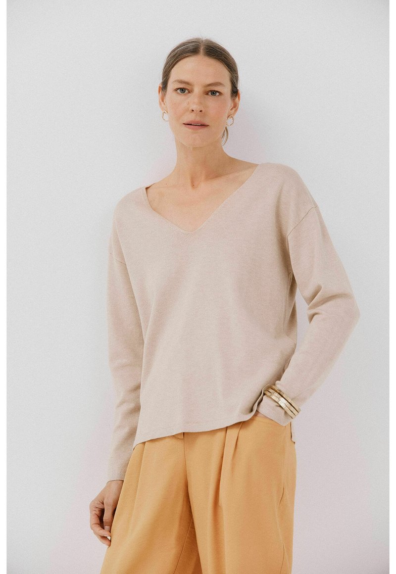 Beige V-hals trui met lange mouwen en een relaxte pasvorm, gemaakt van zachte materialen. Gekleed met losse, lichtoranje broeken.
