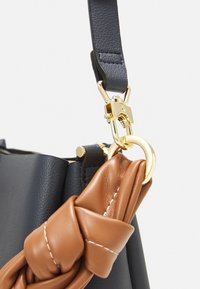 Svart läderhandväska med detaljer som en knutna brun handtag, guldfärgad lås och en slät yta.