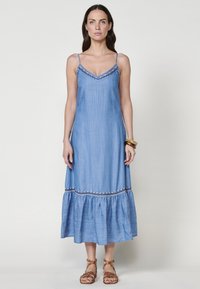 Robe maxi en denim bleu clair avec un corsage ajusté, des bretelles spaghetti et un ourlet à volants, ornée de broderies le long de l'encolure.