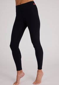 Zwarte leggings met een hoge tailleband, gemaakt van rekbare stof, met contrasterende stiksels en een klein merketiket op de tailleband.