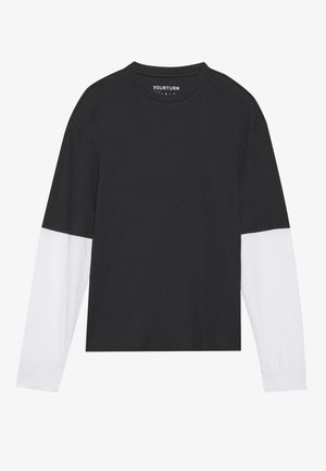Black long-sleeve top with white sleeves, ribbed texture, round neck, and a cropped design. Brand label visible inside the neckline.