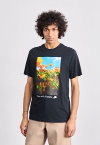 T-shirt preta de algodão com uma estampa gráfica colorida de flores e o texto "Move with Nature" na parte inferior, com um corte descontraído.