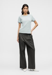 Haut bleu clair à manches courtes avec un col rond, accompagné d'un pantalon sombre à jambes larges et de talons blancs à bout pointu. Textures lisses partout.