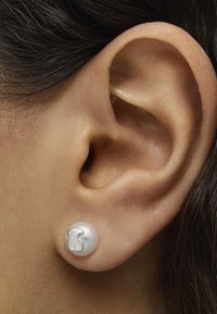 Orecchini a bottone in perla bianca con design di orsetto di gomma. Texture liscia, forma rotonda e dettagli in argento sull'accento dell'orsetto. Indossati all'orecchio.