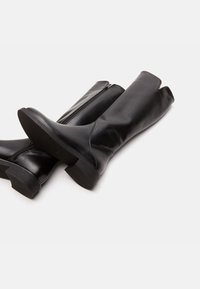 Stivali neri in pelle alti fino al ginocchio con una texture liscia, dotati di cerniera laterale, tacco leggero e design diviso nella parte superiore.