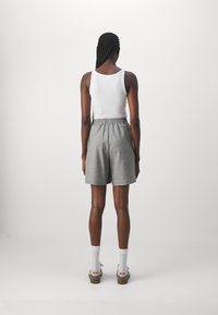 Shorts grigi di lunghezza al ginocchio con una cintura elastica, abbinati a una canotta bianca e calzini leggeri, visti da dietro.