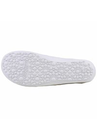White shoe sole with a textured floral pattern and branding detail. Smooth edges with a rounded toe and slight elevation at the heel.