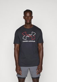 Svart bomullströja med en stor röd och vit Under Armour-logotyp på framsidan, korta ärmar och rund halsringning.
