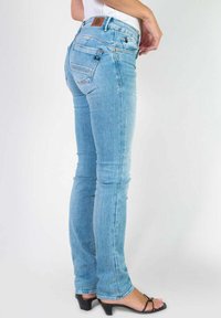Jean skinny bleu clair en denim, avec poches arrière, légère déchirure et design ajusté. Assorti à des sandales à talons noires.