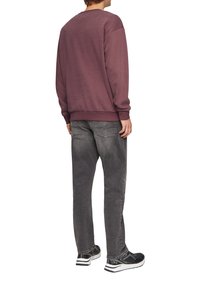 Lila Sweatshirt mit Rundhalsausschnitt, lässiger Passform und gerippten Bündchen, kombiniert mit dunkelgrauen Jeans und schwarzen Sportschuhen mit weißen Akzenten.