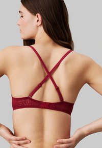 Bralette burdeos con un diseño floral texturizado, tirantes ajustables en forma de cruz y un cierre de gancho y ojo en la parte posterior.