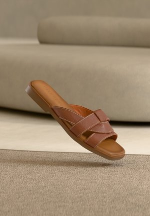 Καφέ δερμάτινο σανδάλι με λουριά που διασταυρώνονται και υφή στην επάνω επιφάνεια. Διαθέτει χαμηλή, επίπεδη σόλα με ανοιχτό σχέδιο στο δάκτυλο.