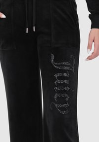 Schwarze Velour-Jogginghose mit weitem Bein, vorderen Taschen und einem mit Strass verzierten Design entlang der Seite, das "Juicy" spell.