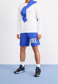 Niebieskie bawełniane szorty z logo "NIKE", w połączeniu z białą koszulą z długim rękawem. Niebieska bluza zarzucona na ramionach. Czarne sneakersy z niebieskimi akcentami.