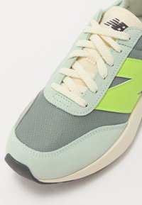 Roheline ja hall sneaker, millel on tekstuuriga võrgusilmast ülemine osa, nahast üleviigud ja erks roheline logo aktsent. Kaasas on kreemjat värvi paelad ja must tall.