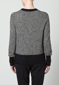 Pull en maille noire et grise avec un corps texturé, un ourlet côtelé noir et des manches contrastantes duveteuses, conçu avec un col rond.