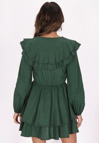 Grünes Baumwollekleid mit Rüschensaum und mehrlagigem Rock, langärmlig mit tailliertem Schnitt. Strukturiertes Detail entlang der Rüschen.