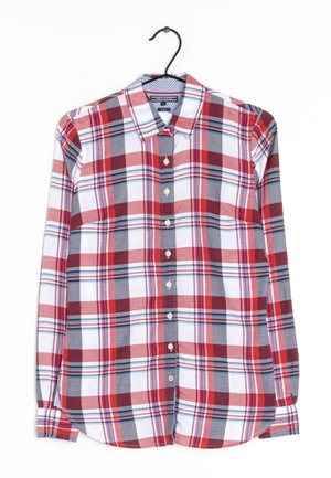 Chemise à carreaux rouges, blancs et gris, à manches longues, boutonnée, sur un cintre noir sur fond blanc.