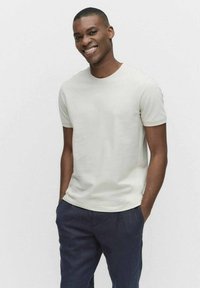 Ljusbeige t-shirt med kort ärm, tillverkad av mjuk bomull, med rund halsringning och en figurnära silhuett, tillsammans med marinblå byxor.