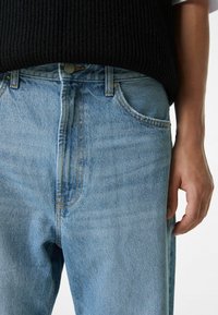 Vaaleansiniset deniminfarkut, joissa on suora leikkaus, ommellut taskut ja napillinen vetoketju. Kangas on hieman teksturoitu ja siinä on haalistuneita yksityiskohtia.