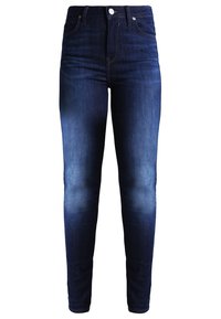 Jeans skinny de corte oscuro en denim, con cintura de media altura, cierre de cremallera y botón, y un leve desvanecimiento en los muslos.