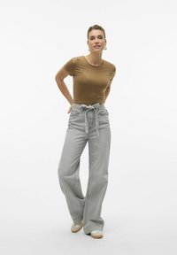 Brun tilpasset t-shirt parret med lysegrå højtaljede bukser med vide ben og en knyttet talje. Modellen har cremefarvede sko på.