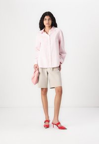 Camicia a righe rosa chiaro e bianca con bottoni, pantaloni corti beige, scarpe con tacco rosso e una borsa a tracolla rosa. Tessuto liscio con una vestibilità comoda.