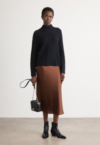 Črn strukturan pulover, rjava satin midi krila, črne gležnjarje in majhna črna torbica z verižnim trakom. Preprost dizajn, kontrastne barve.