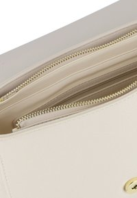 Interno di una borsa in pelle beige con molteplici scomparti con cerniera e cerniere in tono oro, che mostrano una texture liscia e linee pulite.