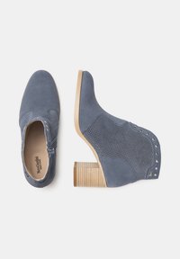 Bottes ankle en suède bleu avec un design perforé, un talon en bois clair et des accents cloutés sur le côté. Elles disposent d'une fermeture éclair sur le côté.