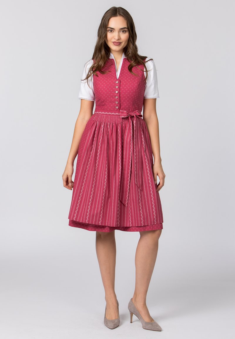 Traditionelles rosa Dirndl mit einem taillierten Oberteil, Knopfverschluss und einem ausgestellt geschnittenen Rock mit einem kontrastierenden Musterdesign. Inklusive passendem Band.
