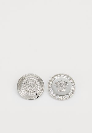 Srebrni okrugli manžetni dugmadi s motivom lavlje glave, okruženi rhinestones i dekorativnim grčkim ključ uzorkom.