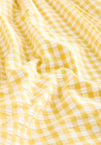 Tessuto a quadretti gialli e bianchi con morbide pieghe e piegature, che evidenziano i dettagli della texture e del motivo.