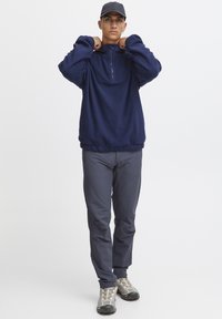 Pullover in pile blu navy con colletto alto, zip a quarto e vita elasticizzata, abbinato a pantaloni grigi a gamba affusolata e scarpe da escursionismo grigie.