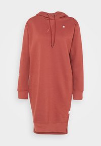 Šaty s kapucí v barvě rzi, s dlouhými rukávy, stahováním na šňůrku, bočními rozparky a malým logem na hrudi. Vyrobené z měkké látky.