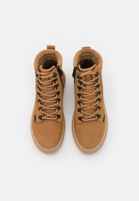 Chaussures hautes marron en cuir et en suède, avec des lacets noirs, une fermeture éclair sur le côté et une semelle en caoutchouc texturée.