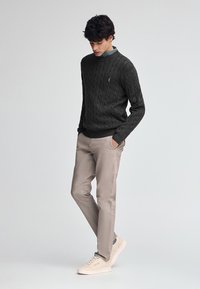 Dunkelgrauer Kabelstrickpullover mit Rundhalsausschnitt, kombiniert mit hellbeigen Slim-Fit-Chinos und hellen Sneakers.