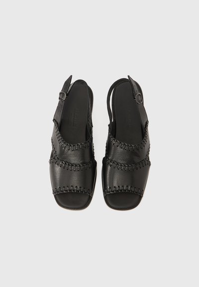 Μαύρα δερμάτινα σανδάλια με σχεδιασμό slingback, που διαθέτουν υφαντή ραφή στα λουριά και λεία, υφή στην επιφάνεια.