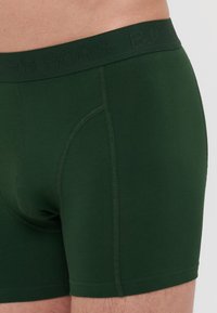Sötétzöld pamut boxeralsó, márkázott, texturált derékpánttal és varrás nélküli kivitelezéssel, amely szoros illeszkedést és sima tapintást biztosít.