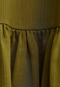 Tela de color verde oliva con una superficie texturizada y acanalada, que presenta pliegues fruncidos a lo largo del dobladillo para añadir volumen y detalle.