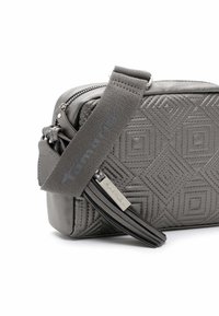 Borsa a tracolla grigia trapuntata con motivi geometrici, cinturino in tessuto regolabile, chiusura con cerniera e tirazip in pelle con marchio.