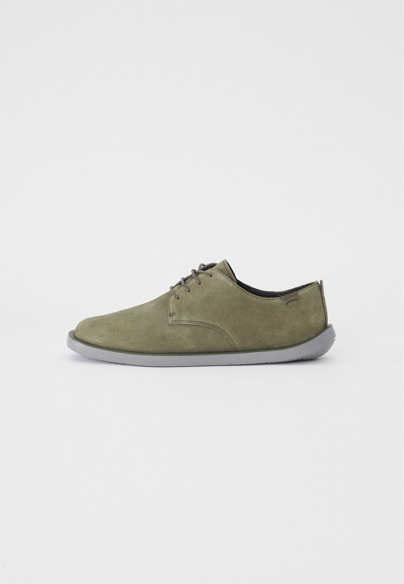 Scarpe in suede verde oliva con una texture liscia, punta arrotondata e suola in gomma grigia. Presentano un design minimal per allacciatura e un accento con il logo.