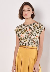 Top de manga corta floral en tela ligera, con un estampado de hojas verde y naranja. Combinado con una falda amarilla con pliegues y un cinturón beige.
