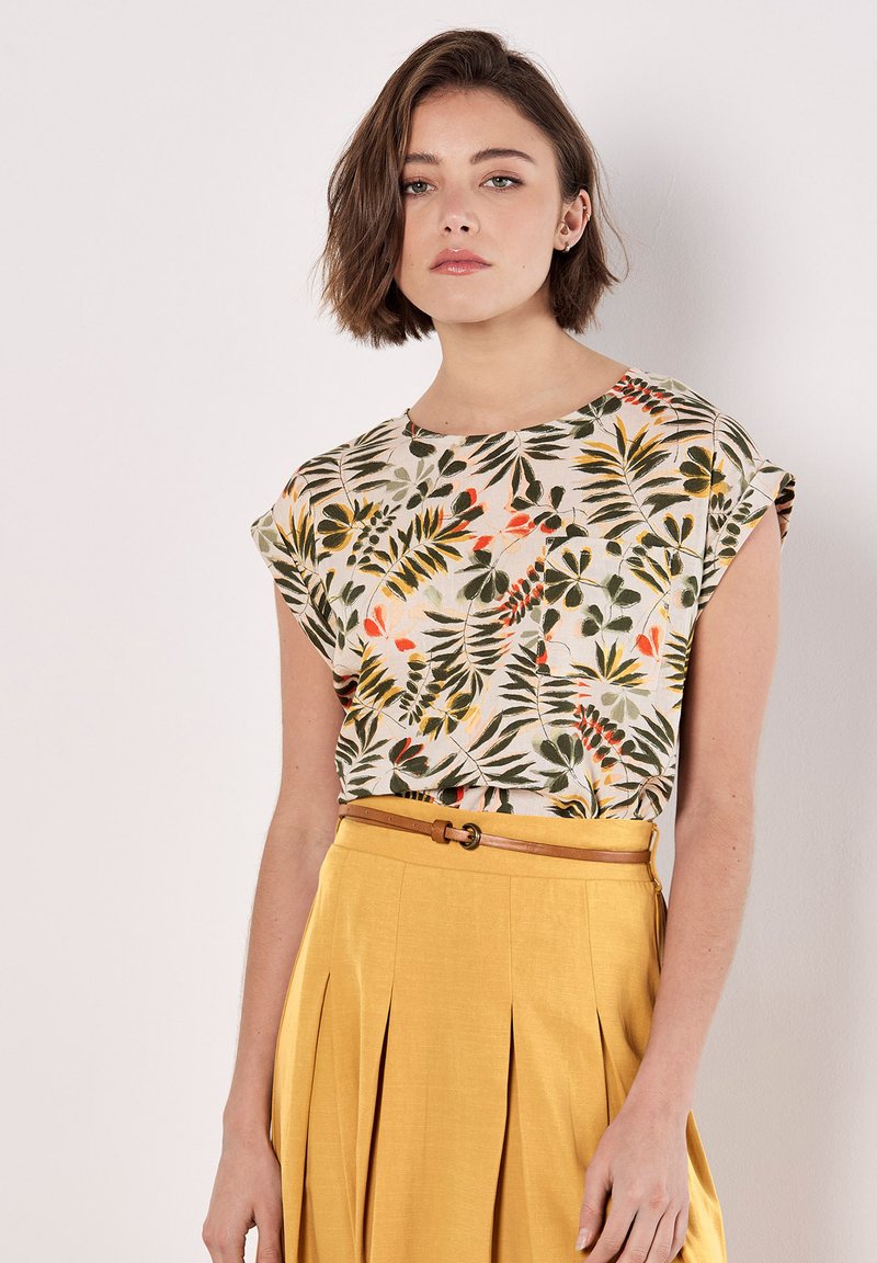 Top de manga corta floral en tela ligera, con un estampado de hojas verde y naranja. Combinado con una falda amarilla con pliegues y un cinturón beige.