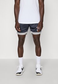 Marine blå mesh idrettsshorts med grå pynt, med en løs passform. Kombinert med en hvit t-skjorte og hvite sokker, båret med svart-hvite sko.