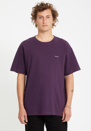 Camiseta de algodón morada con cuello redondo y mangas cortas. Presenta un pequeño logo negro en el lado izquierdo del pecho. Diseño sencillo y corte relajado.
