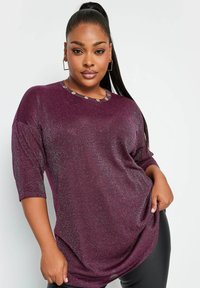 Śliwkowy, brokatowy top z okrągłym dekoltem, ozdobiony złotymi guzikami. Luźny krój i rękawy do łokcia, gładka faktura.