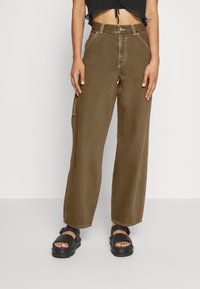 Bruna vida byxor i denim, med framfickor, stickade detaljer och hög midja. Bärs med svarta platåsandaler.